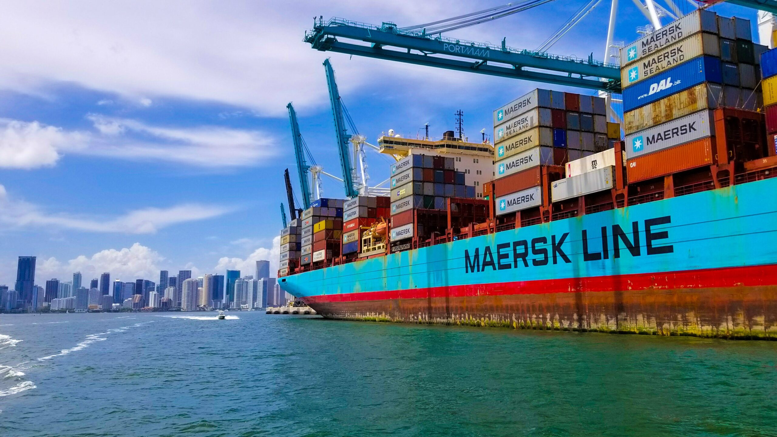 Maersk cargo ship docked at an Indian port with containers being loaded and unloaded.