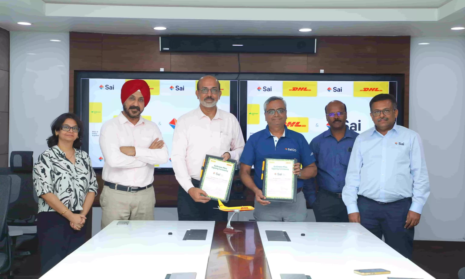 SCM SPECTRUM - DHL and Sai Life Sciences executives shaking hands to mark GoGreen Plus partnership for sustainable logistics.